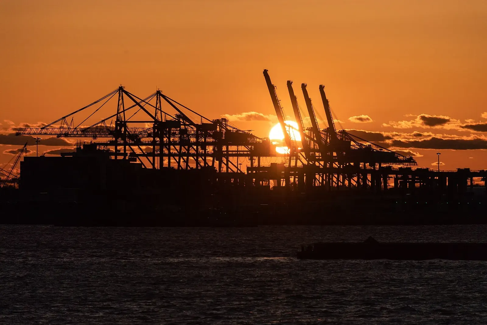 Container cranes at the Port Newark terminal silhouetted against a setting sun